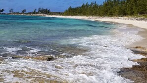 Una playa con agua turquesa cristalina, arena blanca y una zona boscosa al fondo.