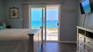 Un dormitorio con cama, televisión y puerta que da a un balcón con vista al océano.
