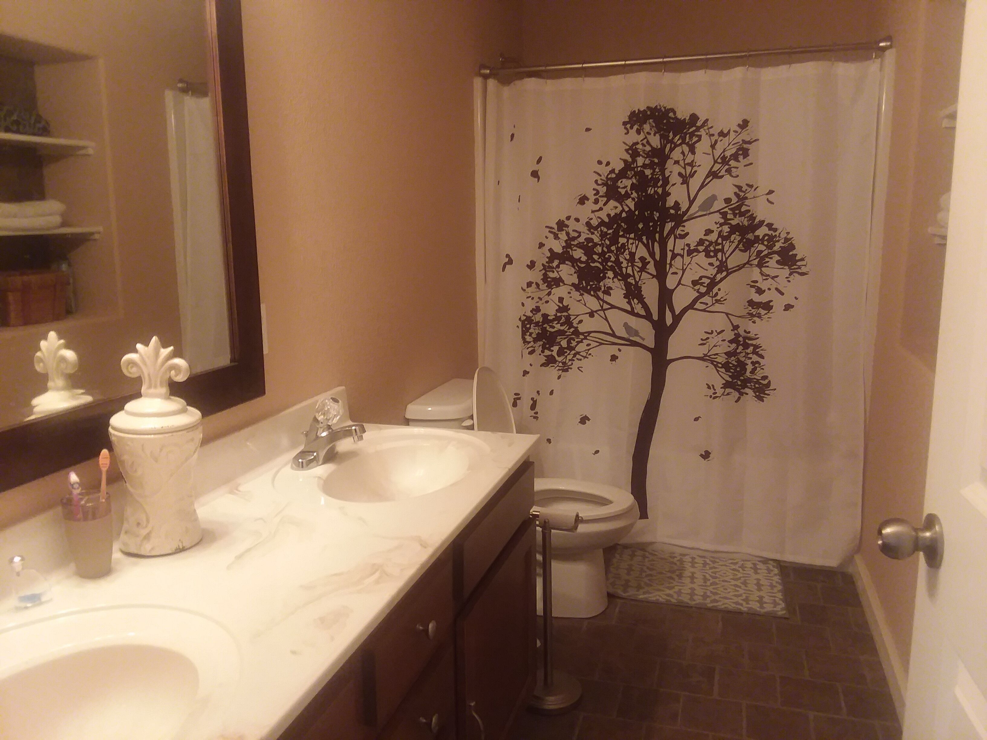 Un baño con lavamanos blanco, un espejo, un inodoro y una cortina de ducha con diseño de árbol.