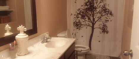 Un baño con lavamanos blanco, un espejo, un inodoro y una cortina de ducha con diseño de árbol.