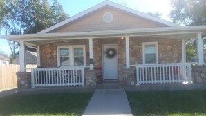 A two-story house with a stone facade, a front porch with white railings, and a front door with a wreath. - 3 Bedroom 2 Bath Bungalow  (Mountain Grove)