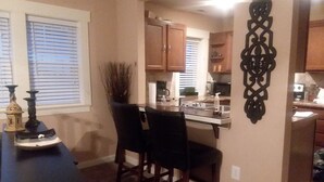 A compact kitchen with a dining area, featuring a small island, dark wooden chairs, and a decorative wall piece. - 3 Bedroom 2 Bath Bungalow  (Mountain Grove)