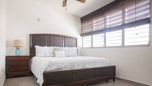 Une chambre à coucher avec un lit en bois, une table de chevet, une lampe et une fenêtre avec des stores.