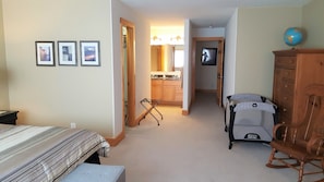 Quarto de hotel com uma cama, penteadeira, cadeira de balanço, mesinha e uma kitchenette ao fundo.