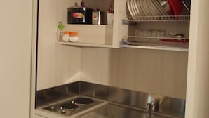 Un angolo cottura compatto con lavello, fornelli e scaffali contenitori.