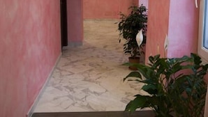 Un corridoio con pareti rosa, pavimento in marmo e piante in vaso.
