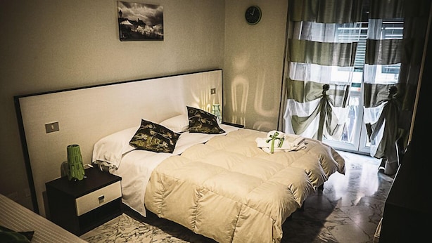 Una camera d'albergo con un letto grande, un comodino, un vaso verde e una finestra con tende.