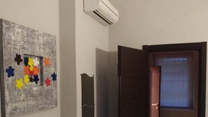 Una stanza con una scrivania in legno scuro, un condizionatore d'aria a muro, un quadro con fiori colorati e una porta che conduce in un'altra stanza.