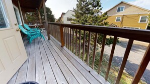 A wooden deck with a railing, turquoise chairs, and a door.