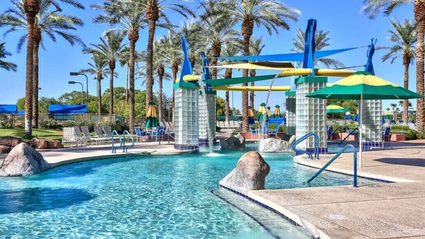 A swimming pool with clear blue water, surrounded by palm trees and lounge chairs.