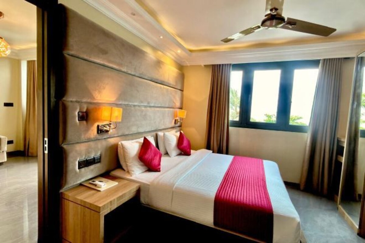 A hotel room with a large bed, bedside lamps, a nightstand, a ceiling fan, and a window with curtains.