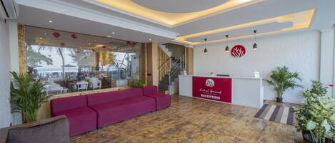 A reception area with a wooden floor, red sofa, and a reception desk labeled "Coral Grand Reception".