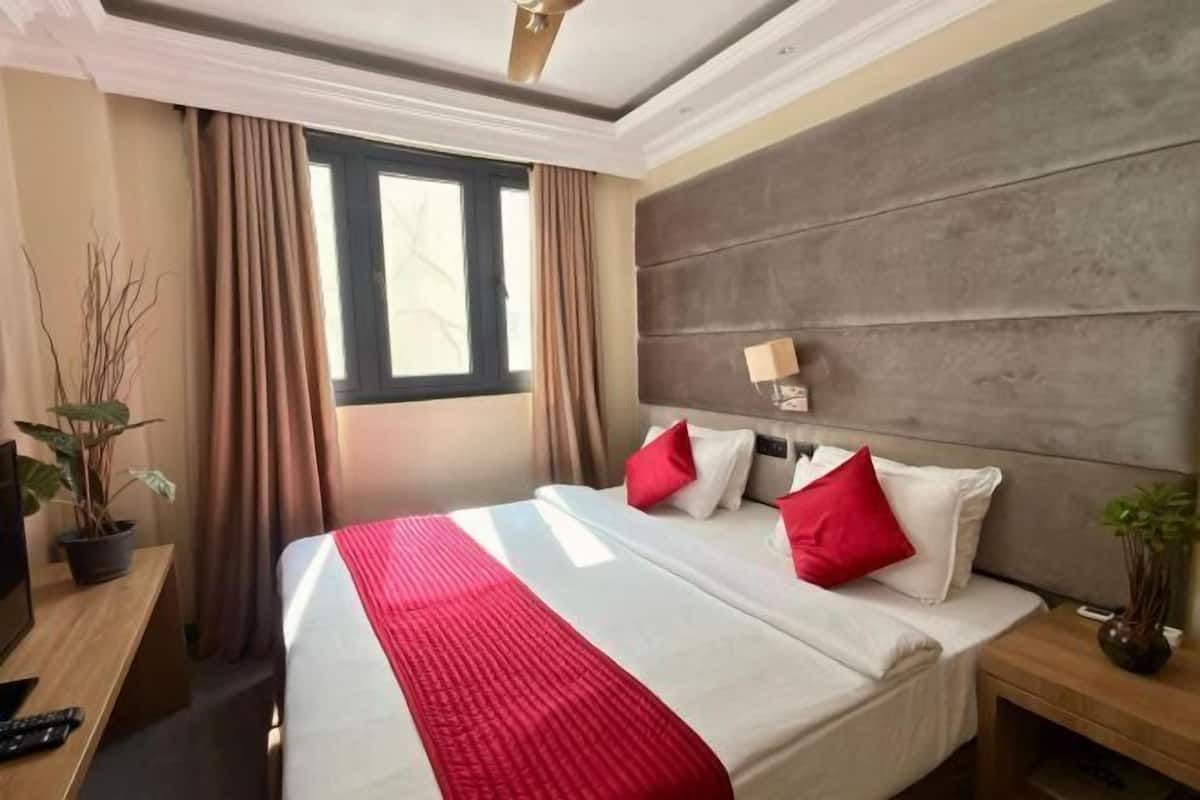 Quarto de hotel com cama grande, cabeceira, mesa de cabeceira, escrivaninha e janela.