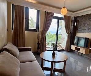 A living room with a sofa, a round table, a TV stand, and a balcony with a view.