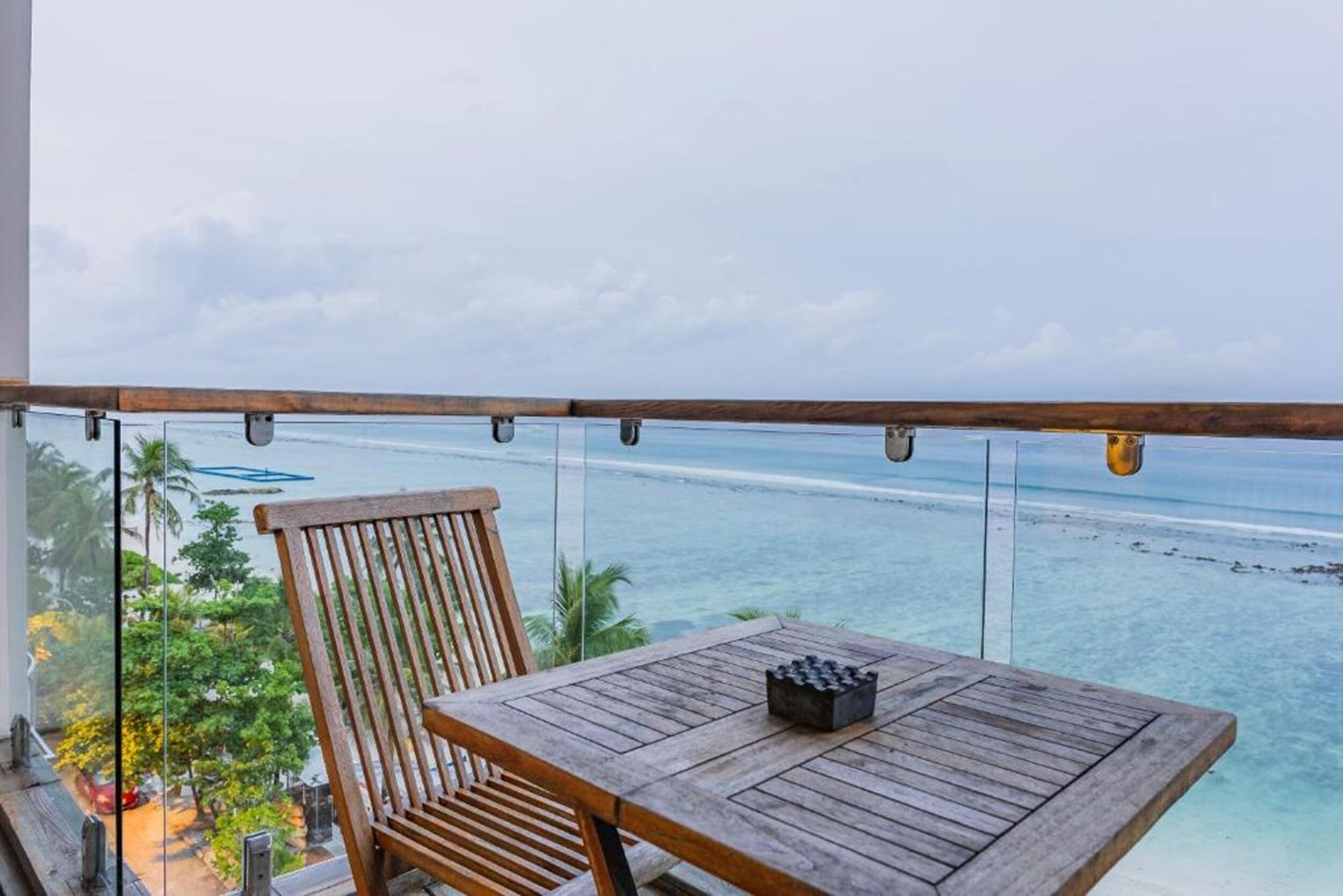 A wooden table and chair on a balcony with a view of the ocean.