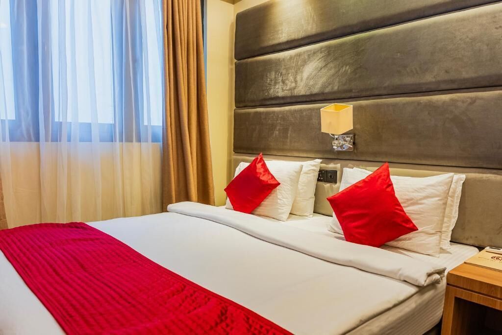 A hotel room with a large bed, a headboard with a light fixture, and a window with curtains.