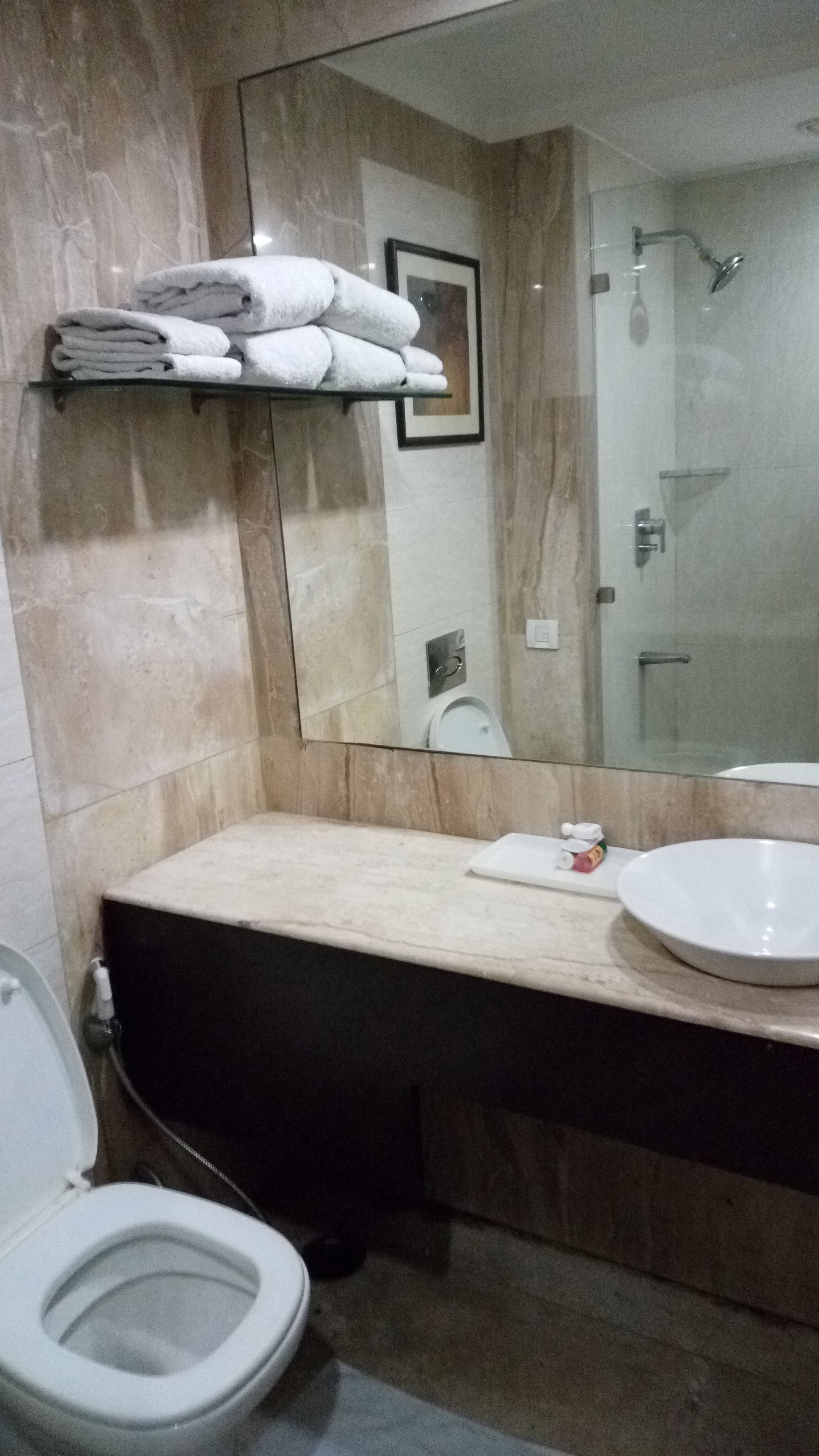 A bathroom with a marble wall, a sink, a mirror, a toilet, and a towel rack with folded towels.