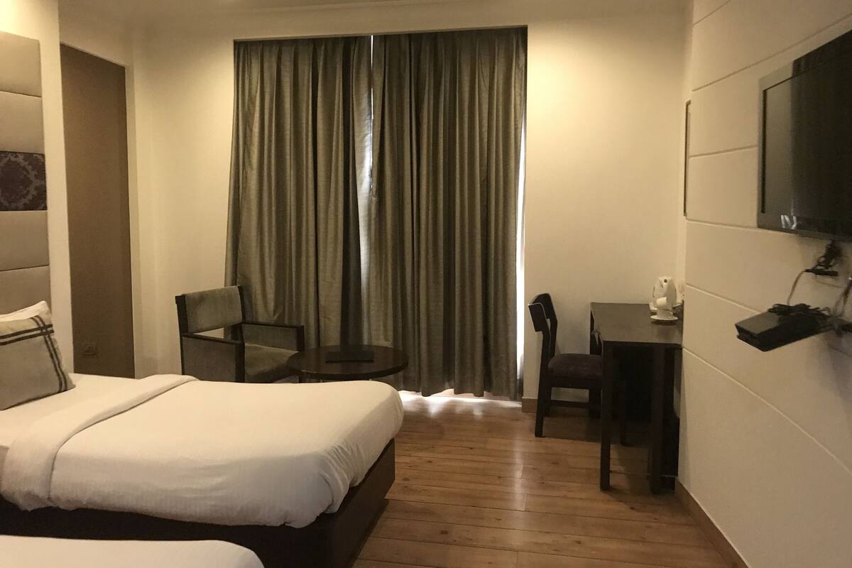 Habitación de hotel con cama, escritorio, silla, televisor montado en la pared y cortina.