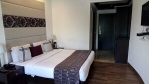 Habitació d'hotel amb llit, taula de nit, làmpada i televisió penjada a la paret.