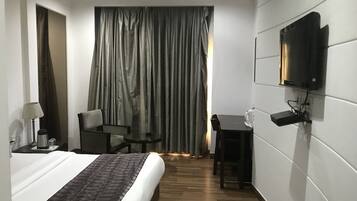 Habitación de hotel con cama, escritorio, silla, televisor en la pared y cortina.