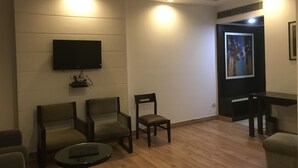Un saló modern amb un televisor de pantalla plana fixat a la paret, dues butaques, una taula petita i un paviment de fusta.