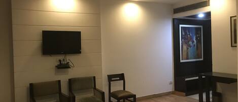 Una sala de estar moderna con una televisión de pantalla plana en la pared, dos sillones, una mesita y suelo de madera.