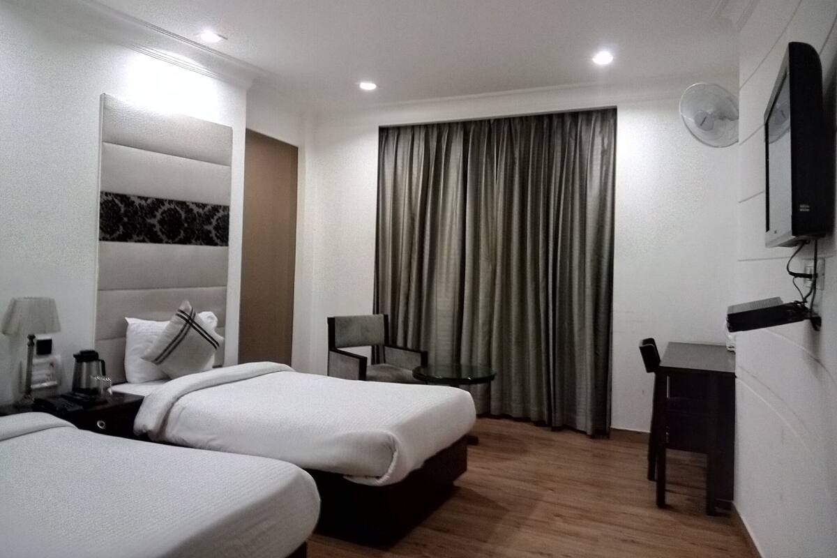 Habitación de hotel con dos camas, un escritorio, una silla, un televisor y una ventana con cortinas.
