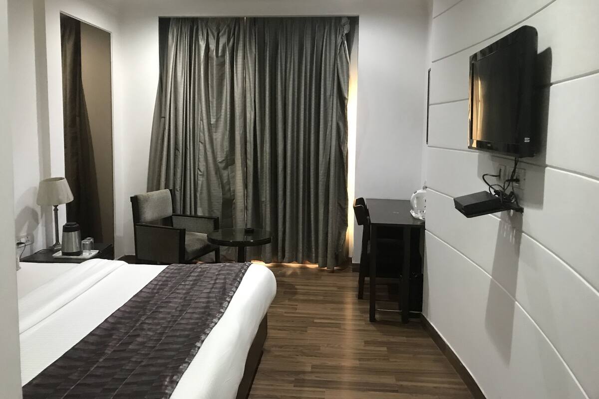 Habitación de hotel con cama, escritorio, silla, televisor montado en la pared y cortina.