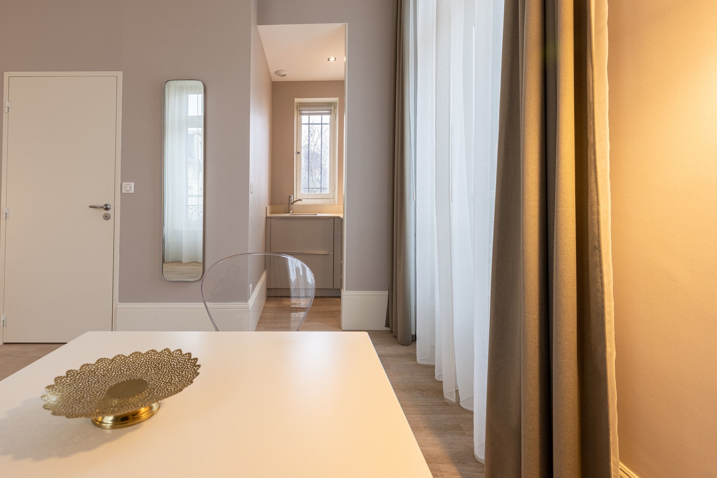 Un interior moderno con una puerta blanca, un espejo, una mesa de vidrio y vistas a un baño con ventana.