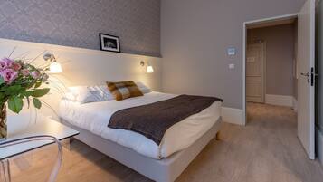 A modern bedroom with a bed, bedside lamps, a small table, and a plant.