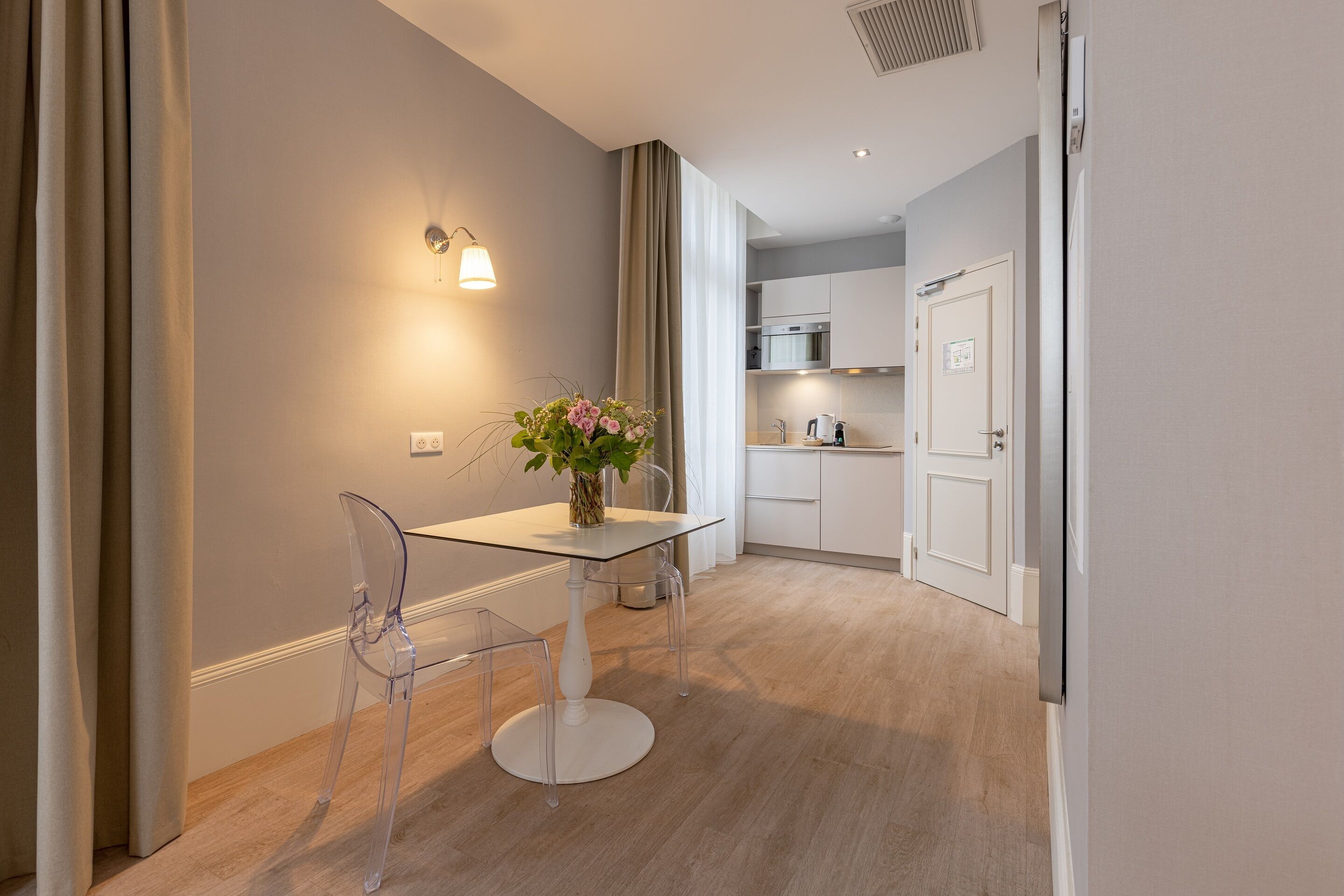 Een moderne keuken met witte kasten, een oven van roestvrij staal en een eethoek met een glazen tafel en stoelen.