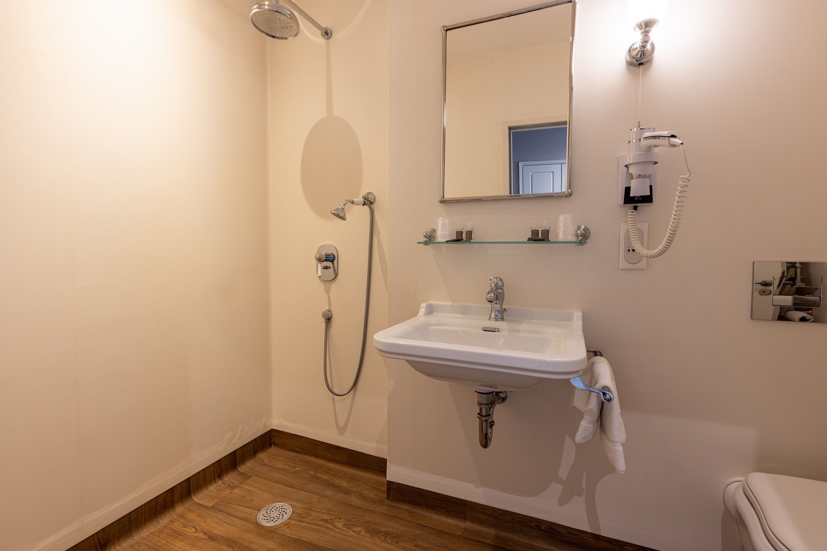 Un baño con ducha, lavamanos, espejo y toallero.