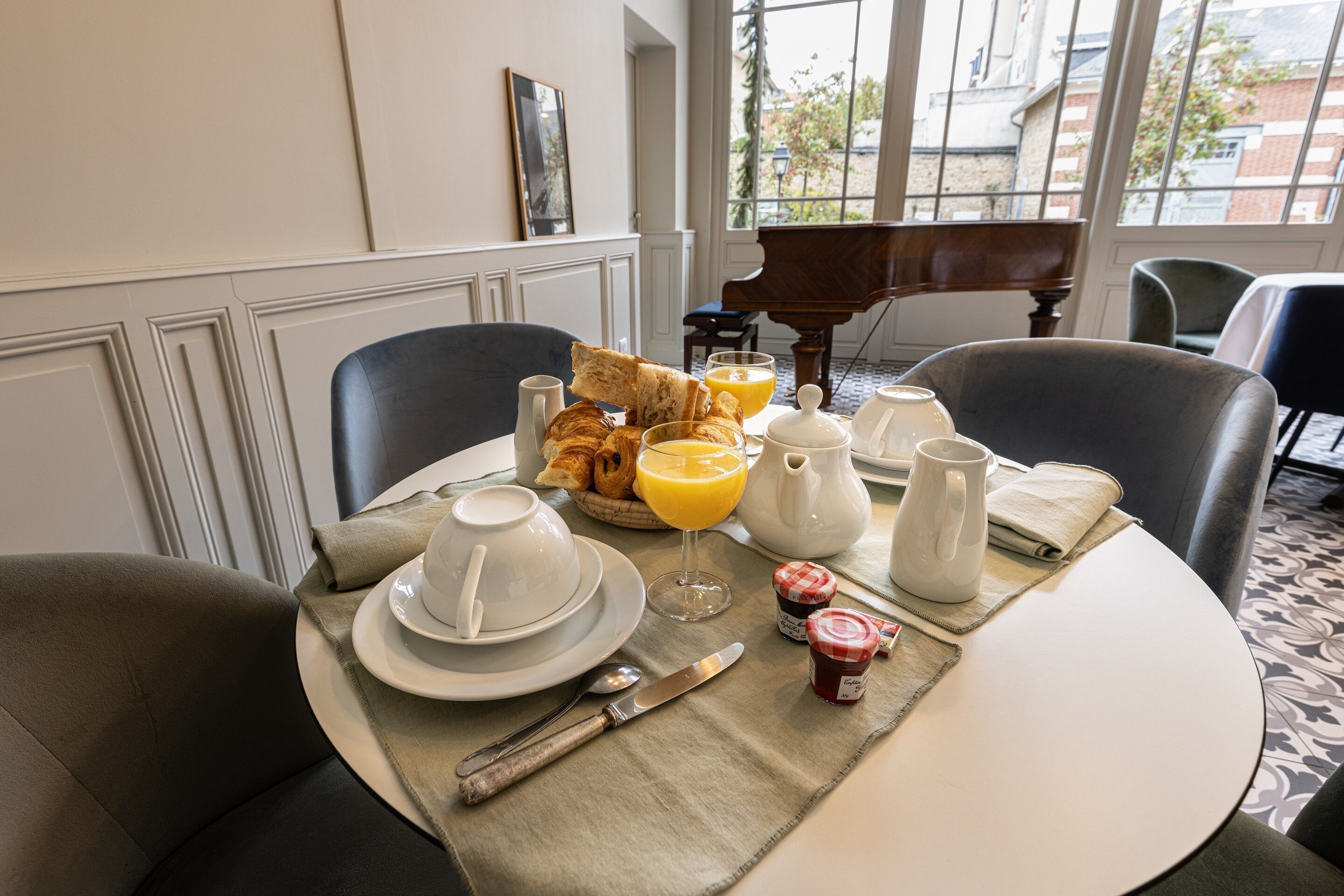 A breakfast setting with a table set for two, including croissants, orange juice, and a coffee pot.
