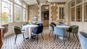 Un espace repas avec des tables et des chaises, de grandes fenêtres et un mur en pierre.