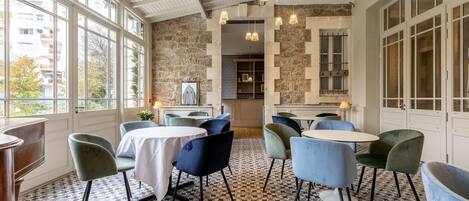 A dining area with tables and chairs, a patterned floor, and a stone wall.