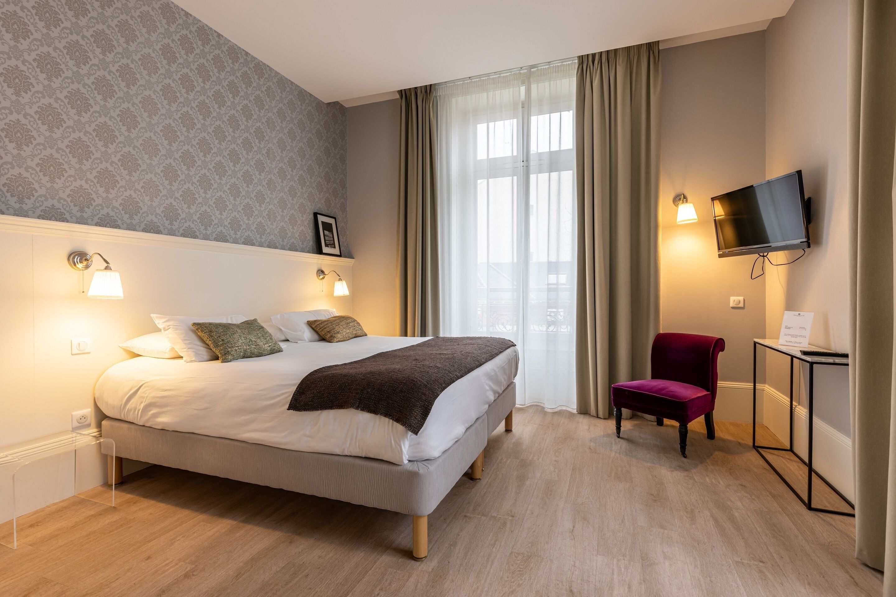 Una habitación de hotel moderna con una cama grande, dos lámparas de noche, un televisor, una silla y un escritorio con una lámpara.