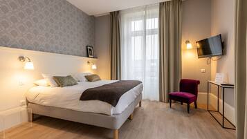 Una habitación de hotel moderna con una cama grande, dos lámparas de noche, un televisor, una silla y un escritorio con una lámpara.