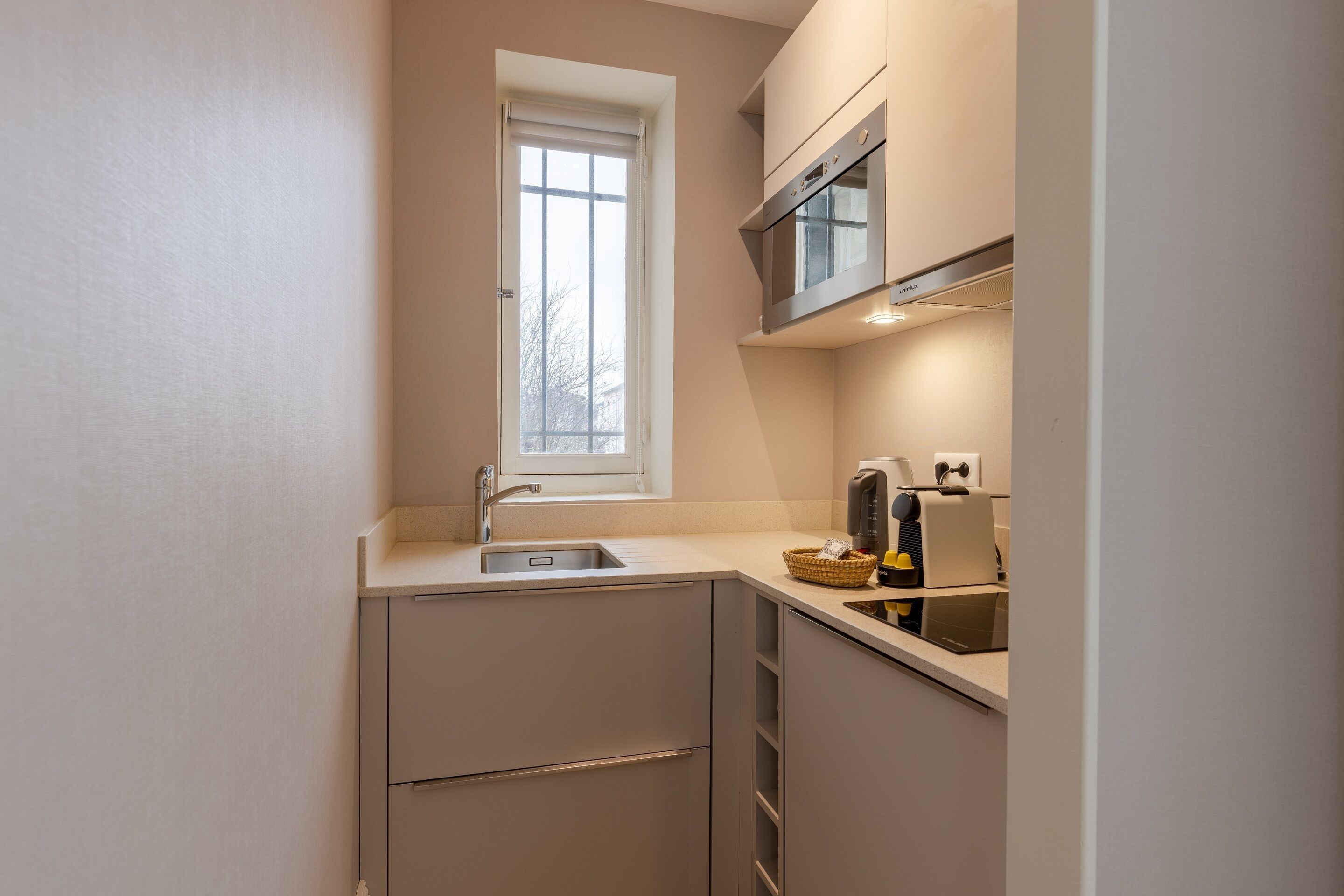 Eine kompakte Küche mit Fenster, einer eingebauten Mikrowelle und einer Kaffeemaschine.