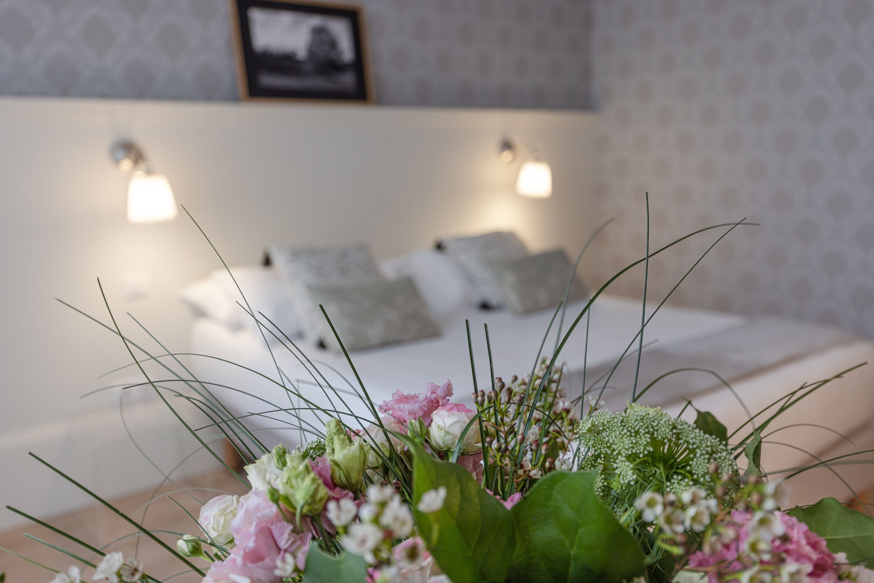 A neatly made bed with pillows and a floral arrangement in the foreground.