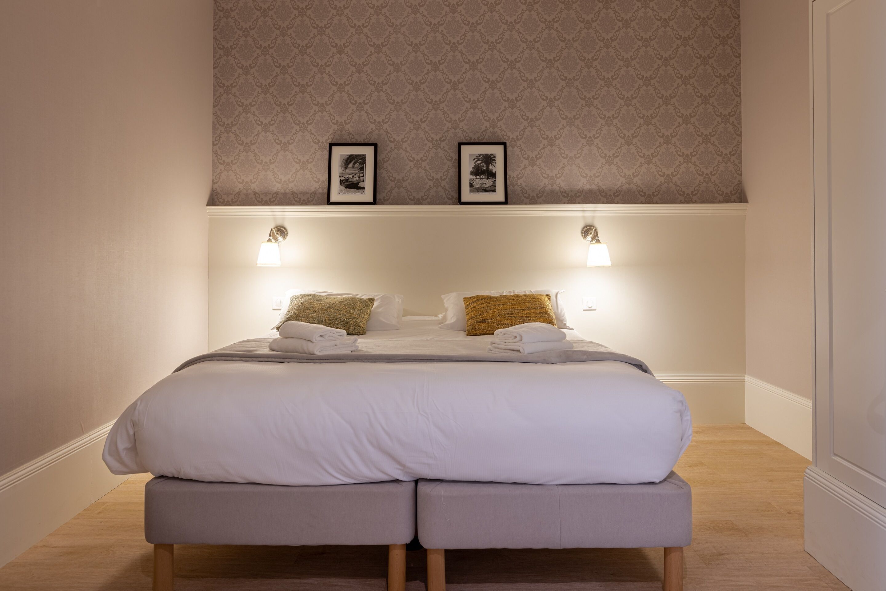 A double bed with a headboard, two wall-mounted lamps, and two framed pictures on the wall above.