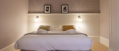 A double bed with a headboard, two wall-mounted lamps, and two framed pictures on the wall above.
