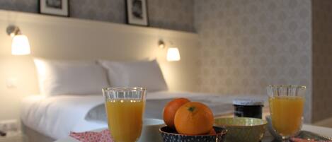 A breakfast tray with orange juice glasses, a bowl of oranges, and a decorative tray in a hotel room with a bed and wall-mounted lights.