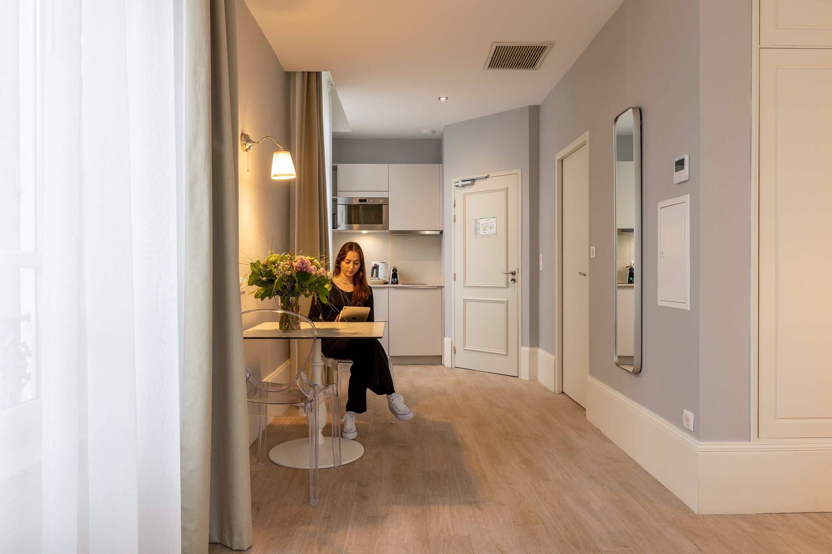 A modern kitchen with a built-in oven and microwave, a dining area with a table and chairs, and a hallway with a door and a mirror.