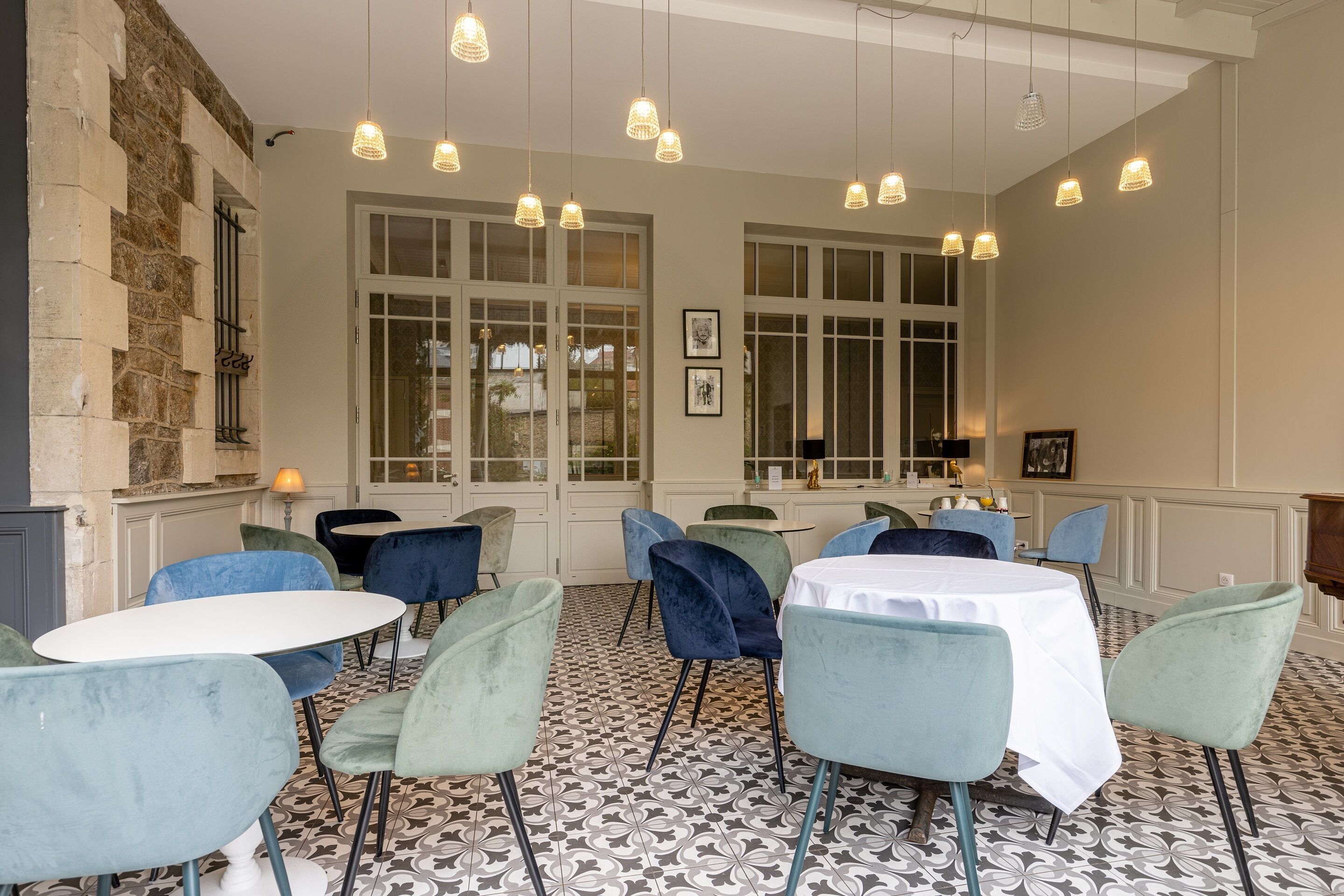 Uma sala de jantar com mesas e cadeiras redondas, janelas amplas e luminárias pendentes.