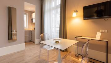 A modern hotel room with a dining area, a TV mounted on the wall, and a view of the city.