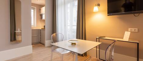 A modern hotel room with a dining area, a TV mounted on the wall, and a view of the city.