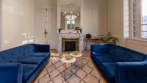 Une pièce avec deux canapés bleus, une cheminée, un lustre et un grand miroir.