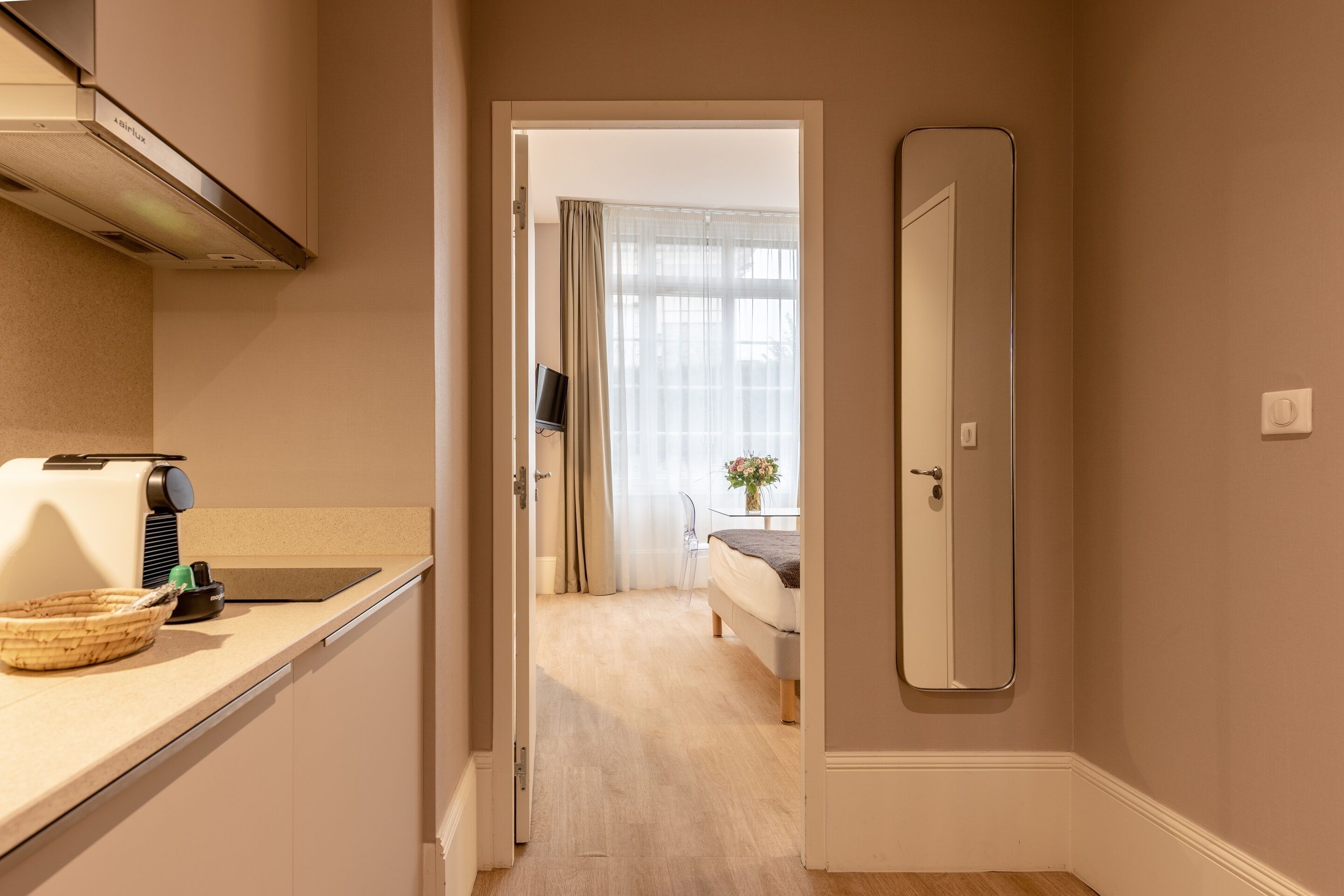 Un pasillo estrecho que conduce a un dormitorio con cama, televisor y ventana con cortinas.