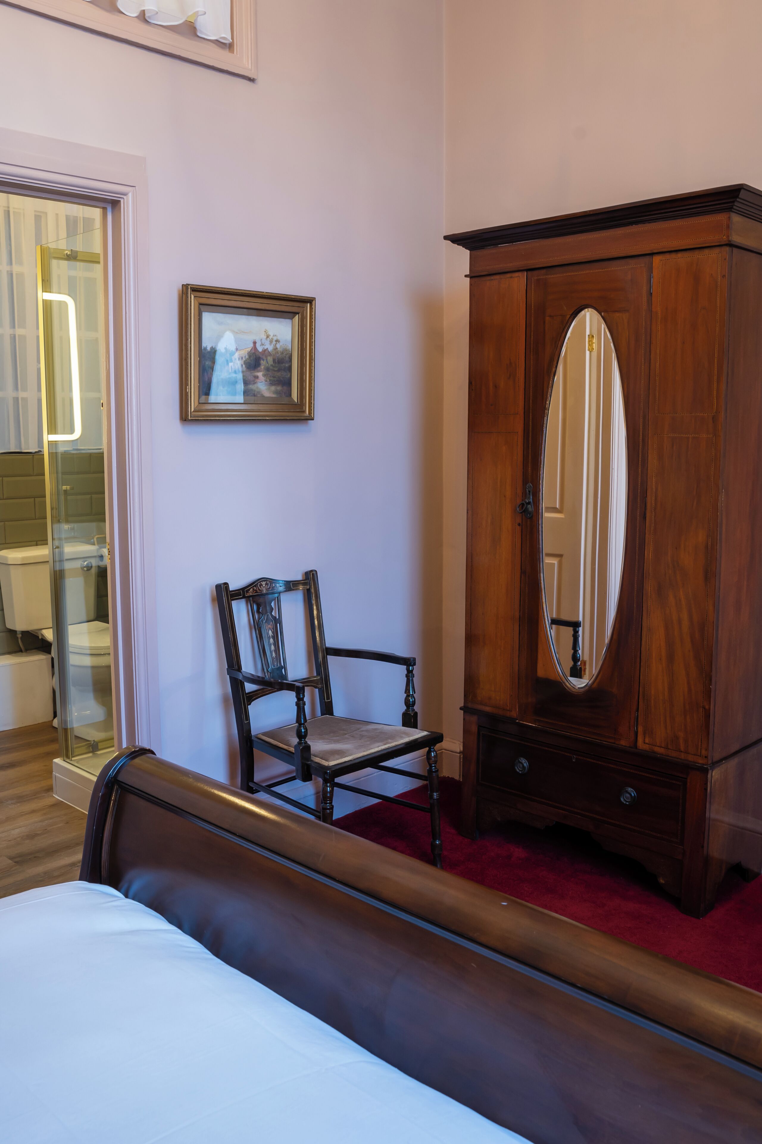Un dormitorio con una cama, un armario de madera con espejo, una silla y un cuadro en la pared.