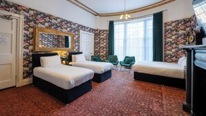 A hotel room with two beds, a large mirror, a clock, and a floral wallpaper. - City Studios - Rodney Street (Liverpool)